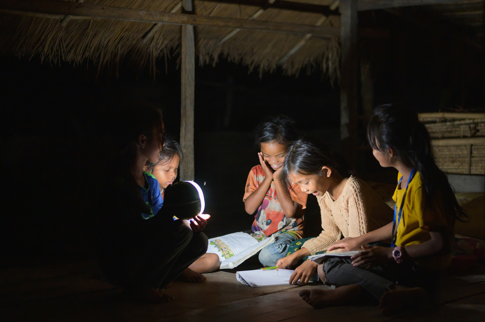 Photo: Children singing with open music textbooks, all under the light of solar lanterns